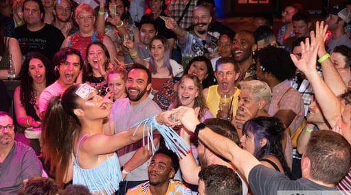 drag performer with dollar bill stuck to forehead in the middle of a crowd accepting tips 