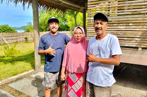 Owners of Afulu Surf Resort smiling on the beach with surf in the background.