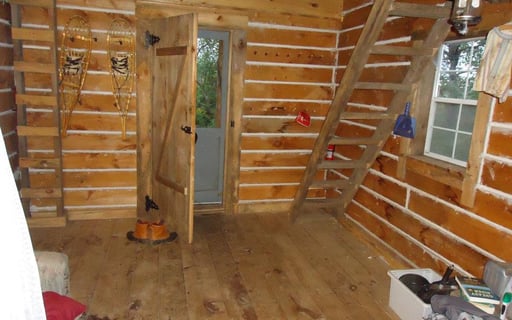 the inside of the log cabin with a ladder leading up to an unseen loft