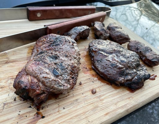 Ribeye and new york strip steaks cooked over coals caveman style