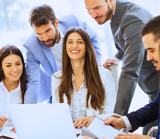 Seated leader smiles at the camera while using her laptop. Three others look at her screen, and two focus on their own tasks