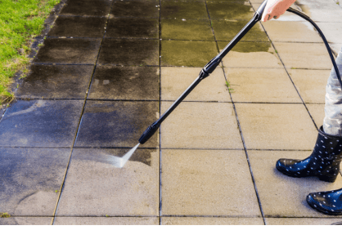 Pressure washing dirty concrete patio tiles to remove grime and restore a clean surface