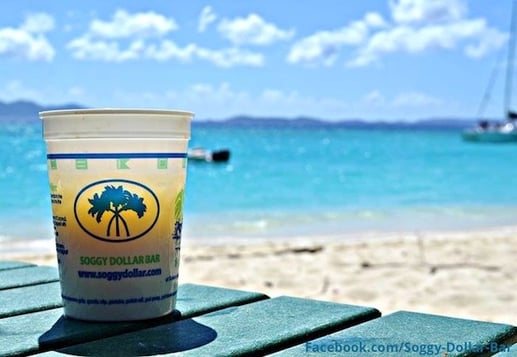 a yellow beach cocktail sits in a cup on the arm of a beach chair, overlooking the sea