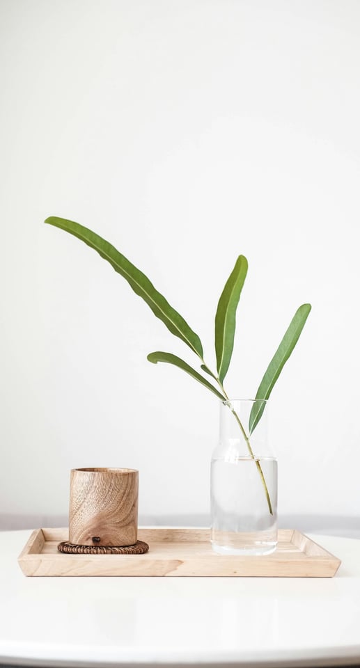 Un plateau en bois avec dessus un verre en bois et un vase rempli d'eau et d'une branche verte