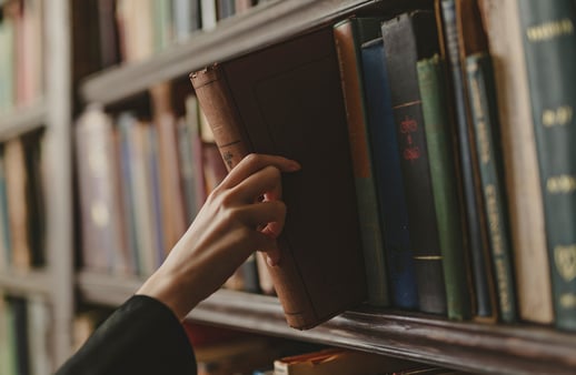 Hand reaching for a vintage book on a library shelf lined with books