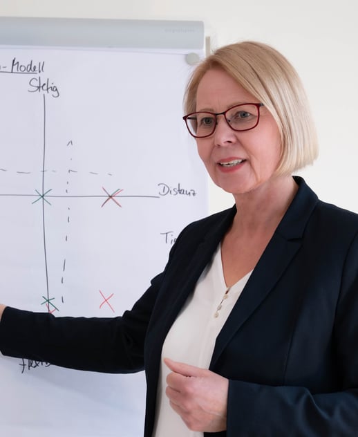 a woman in a business suit is holding a pen and pointing at a white board