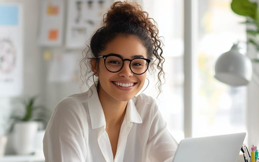Emprendedora joven sonriente trabajando en laptop, representa productividad y liderazgo femenino en negocio digital en casa.