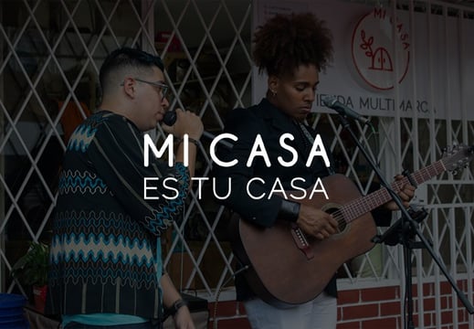 Imagen del día de inauguración de MI CASA, Tienda Multimarca, con dos cantantes locales de fondo y el slogan de la tienda.