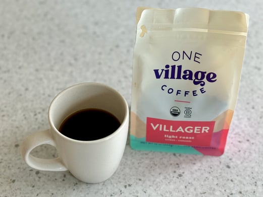 A cup of black coffee in a white cup sitting next to a bag of coffee beans