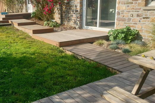  Terrasse en bois aménagée par AJ Paysagiste devant une maison en pierre avec jardin fleuri