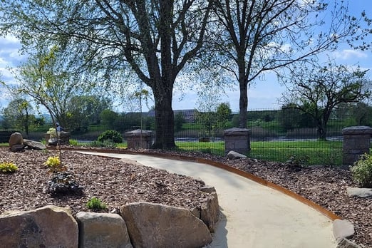 Allée dallée en béton décoratif dans un jardin paysager avec arbres et massifs végétalisés