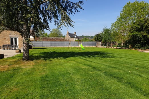 Pelouse parfaitement tondue dans un jardin paysager ensoleillé avec une maison en arrière-plan