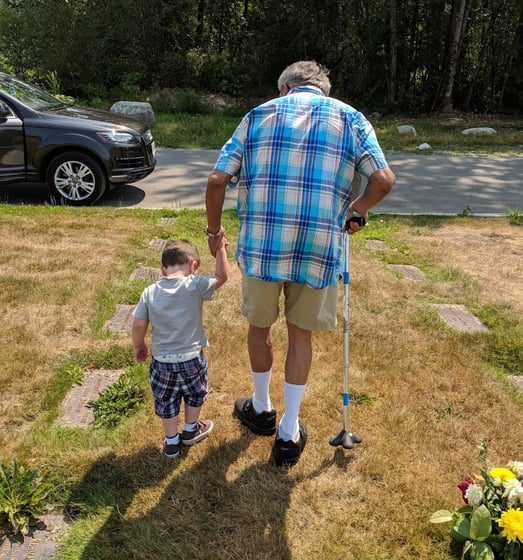An older man with a cane walks with a small child at a cemetary