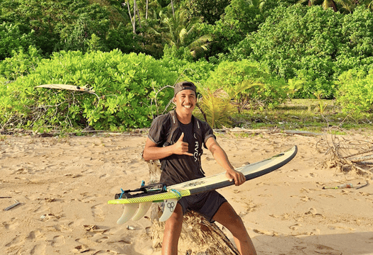 Dicky, surf guide at Afulu Surf Resort, posing with a surfboard on the beach.