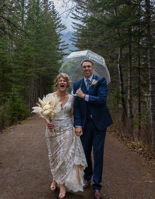 Bride and groom walking down a path in the woods in Banff