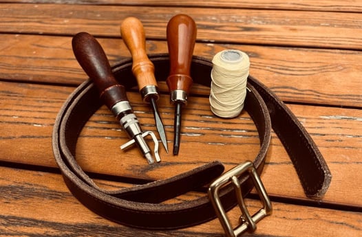 a leather belt strap with a thread spools and leather tools