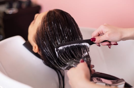 Hair stylist applying keratin treatment to woman's hair in salon
