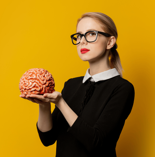 a blond woman with black glasses, holding a brain. she's on a yellow background.