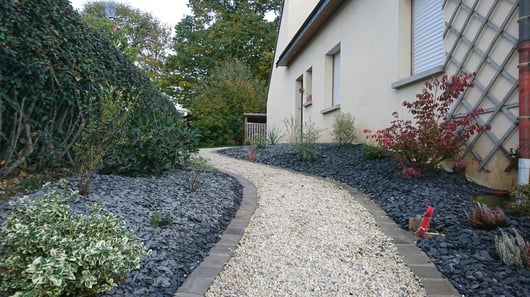 Allée en gravier clair bordée de pas japonais et de massifs paysagers le long d'une maison
