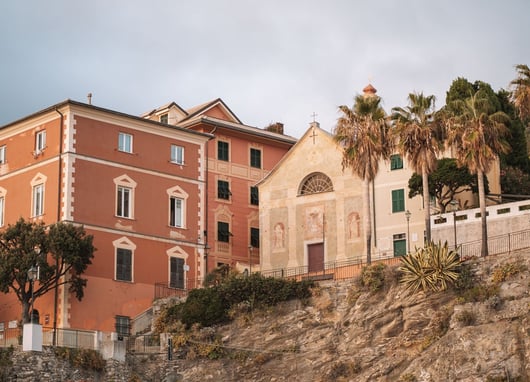 Palm trees - faded frescoed church - terracotta-hued buildings on rocky hillside - Bogliasco