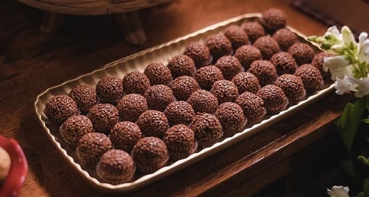 Uma bandeja cheia de brigadeiros de chocolate cuidadosamente dispostos sobre uma mesa de madeira, ce