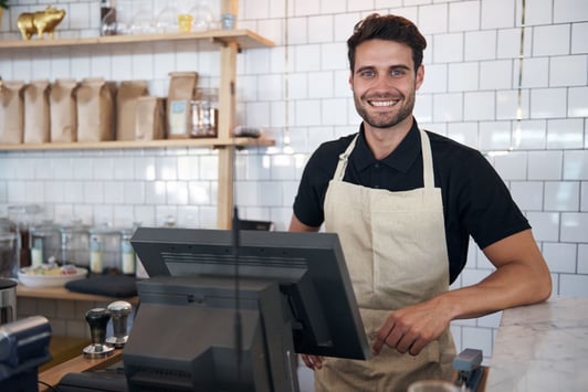 A happy store owner works at his coffee shop's point of sale system.