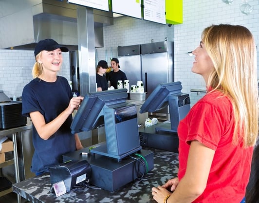 A customer orders off of a menu while the worker takes her order on a point of sale machine.