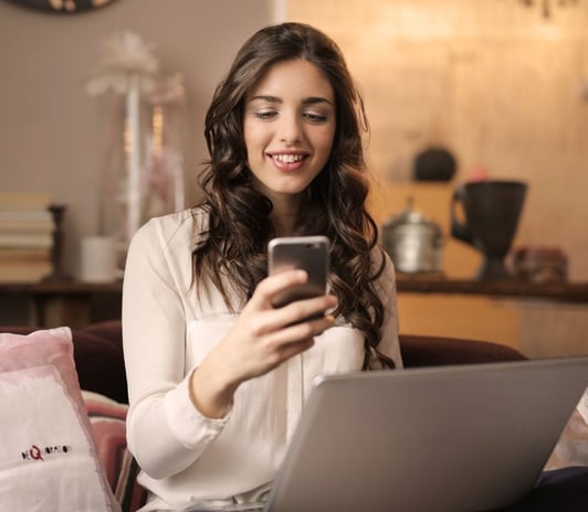 a woman sitting on a couch with a laptop and a cell phone