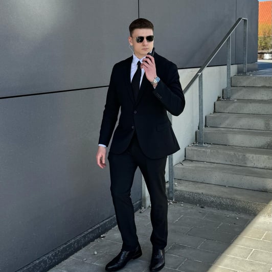 Sicherheitsmitarbeiter in Anzug mit Headset vor grauem Gebäude.