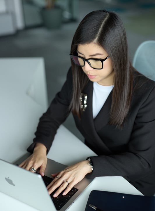 Ka Ming Zwingenberger in a suit and glasses is typing on a laptop on a desk.