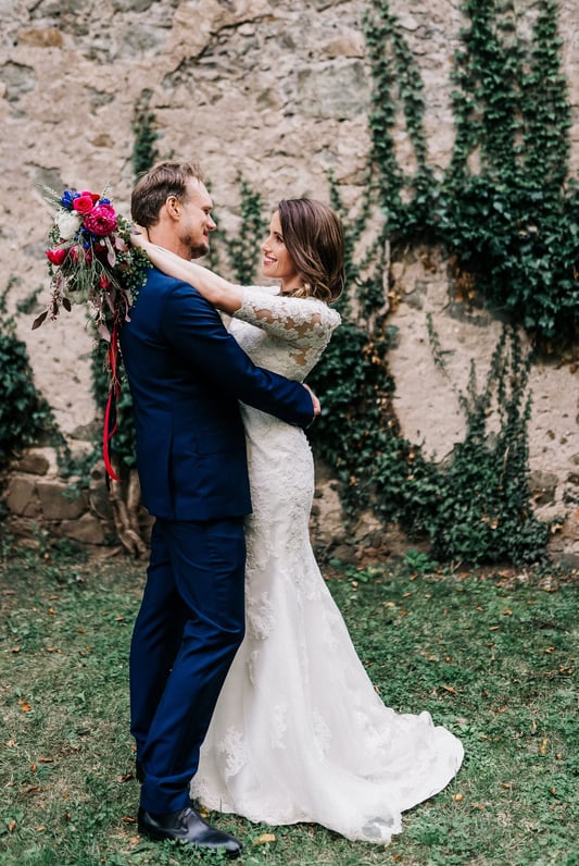 a bride and groom standing in front of a stone wall