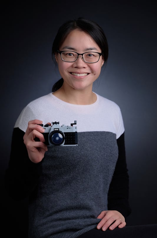 a woman in glasses and a sweater holding a lego camera