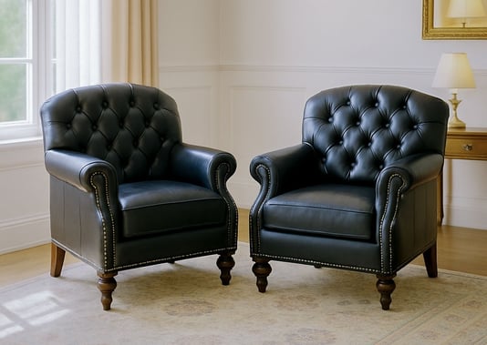 Two tufted black leather armchairs in a bright living room with soft drapes, sconces, and mirror.