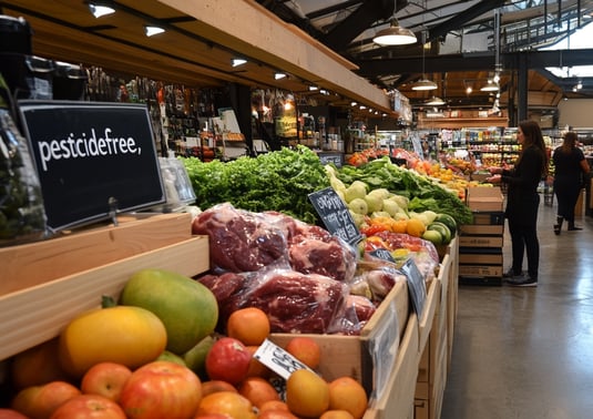 a man standing in a store with a lot of fruit and vegetables
