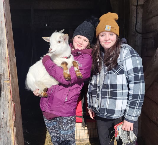 two young girls standing together one of them is holding a white goat