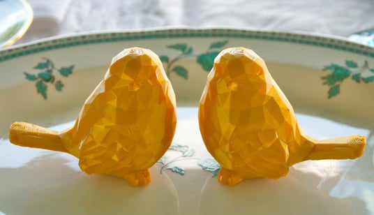 two golden bird ornaments sitting on a plate as wedding decoration