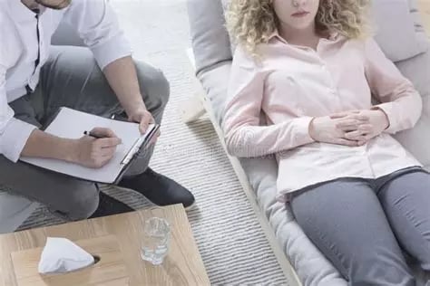 Femme allongée en relaxation mains sur le ventre à côté de son thérapeute qui prend des notes