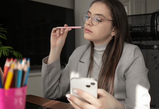 a woman in glasses and a gray sweater is holding a cell phone