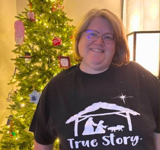 a customer wearing a joyhelpers t-shirt standing in front of a Christmas tree.