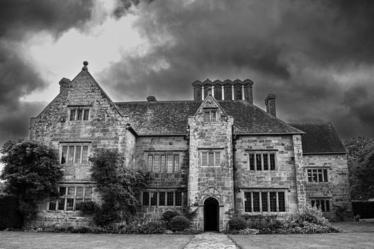 A black & white photos of National Trust Batemans set against stormy looking clouds.