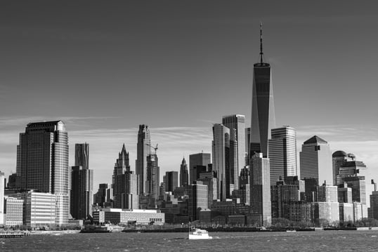 A black and white photo of New York City skyline taken from the Hudson River. in the forground is a pleasure boat passing