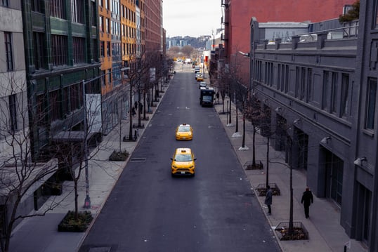 two yellow taxis drive down the centre of an empty new york city street