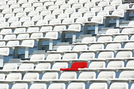 a red chair in a stadium with many white chair