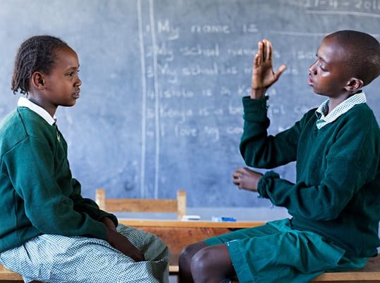 An image of 2 kids signing at each other in a classroom