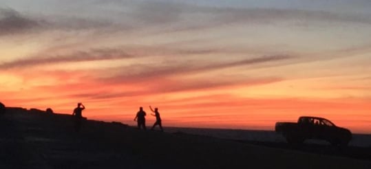 A picture showing an enchanting silhouette of three people being playful while enjoing the sunset.