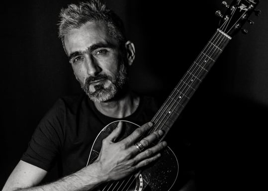un homme tient une guitare dans ses bras et regarde l'objectif