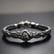 A collection of intricately designed metallic jewelry pieces in various shapes, featuring floral and leaf motifs. The pieces are adorned with small, round, deep green beads scattered on a textured dark surface.