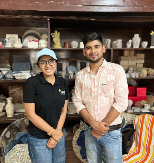 Team member and artisan standing in front of a shelf of gaurahari products.