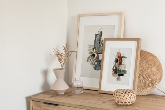 2 framed abstract mixed media art prints by Sweet Ruby Moon styled with neutral decor on a light wood dresser