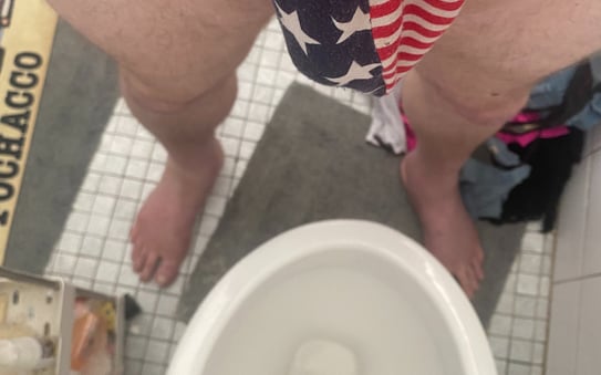a man wearing a g-string that has a USA flag pattern while standing in front of a toilet